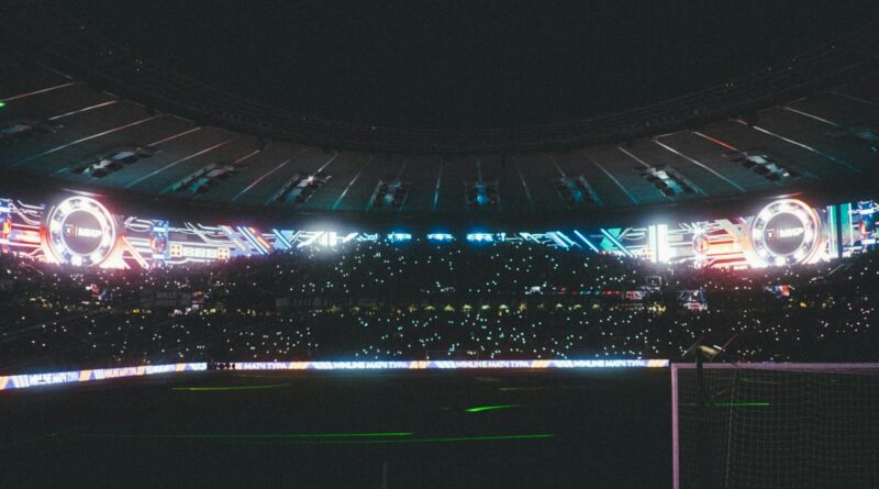 A packed football stadium glowing under bright floodlights at night, the backdrop to the 2026 Ballon d'Or race