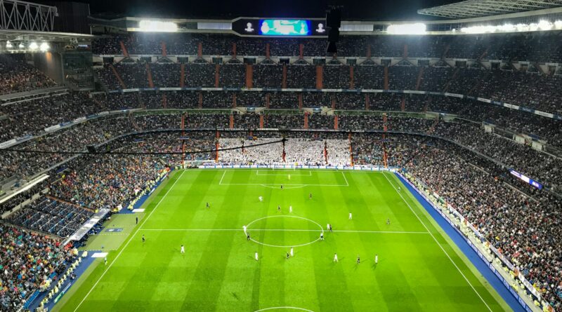 Football match under floodlights in a packed stadium, illustrating the summer 2026 transfer battle for Rodri