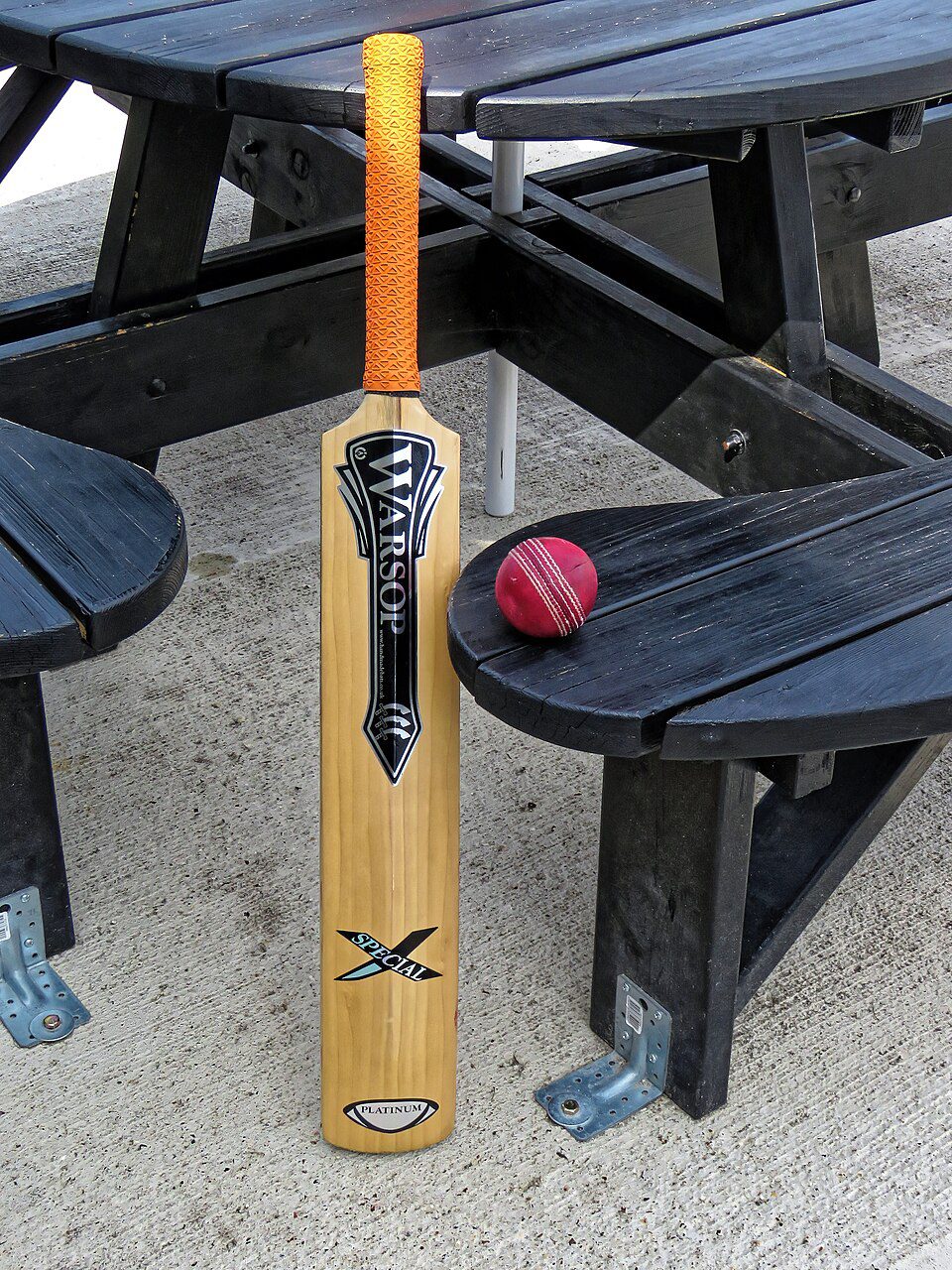 Cricket bat and red ball on an outdoor table